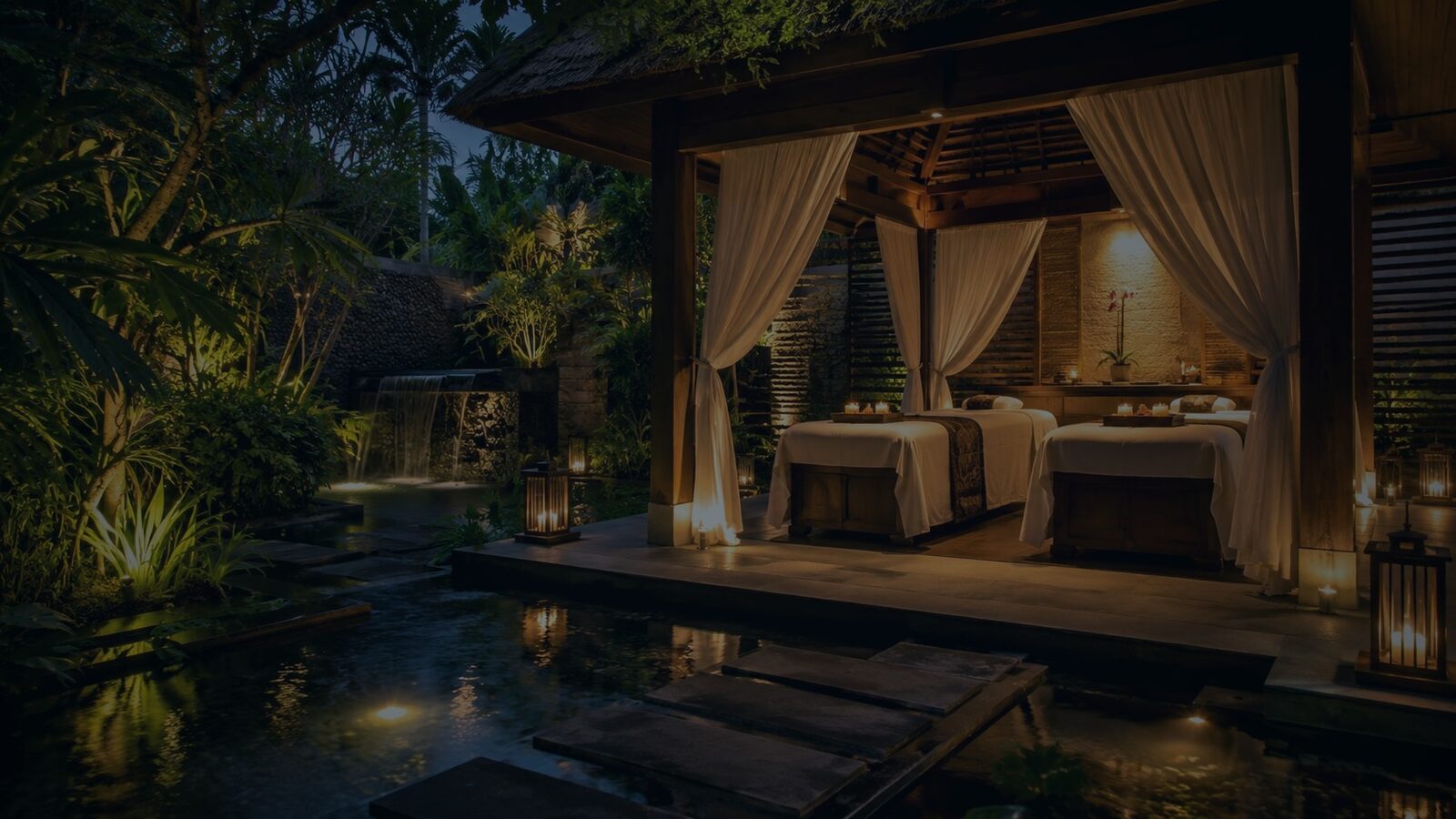 Candlelit garden spa pavilion with treatment beds beside a water feature